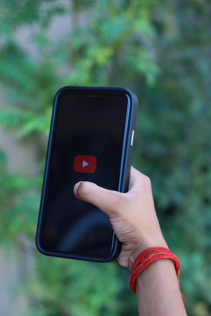 Hand holding smartphone with YouTube logo against a green background, outdoors.